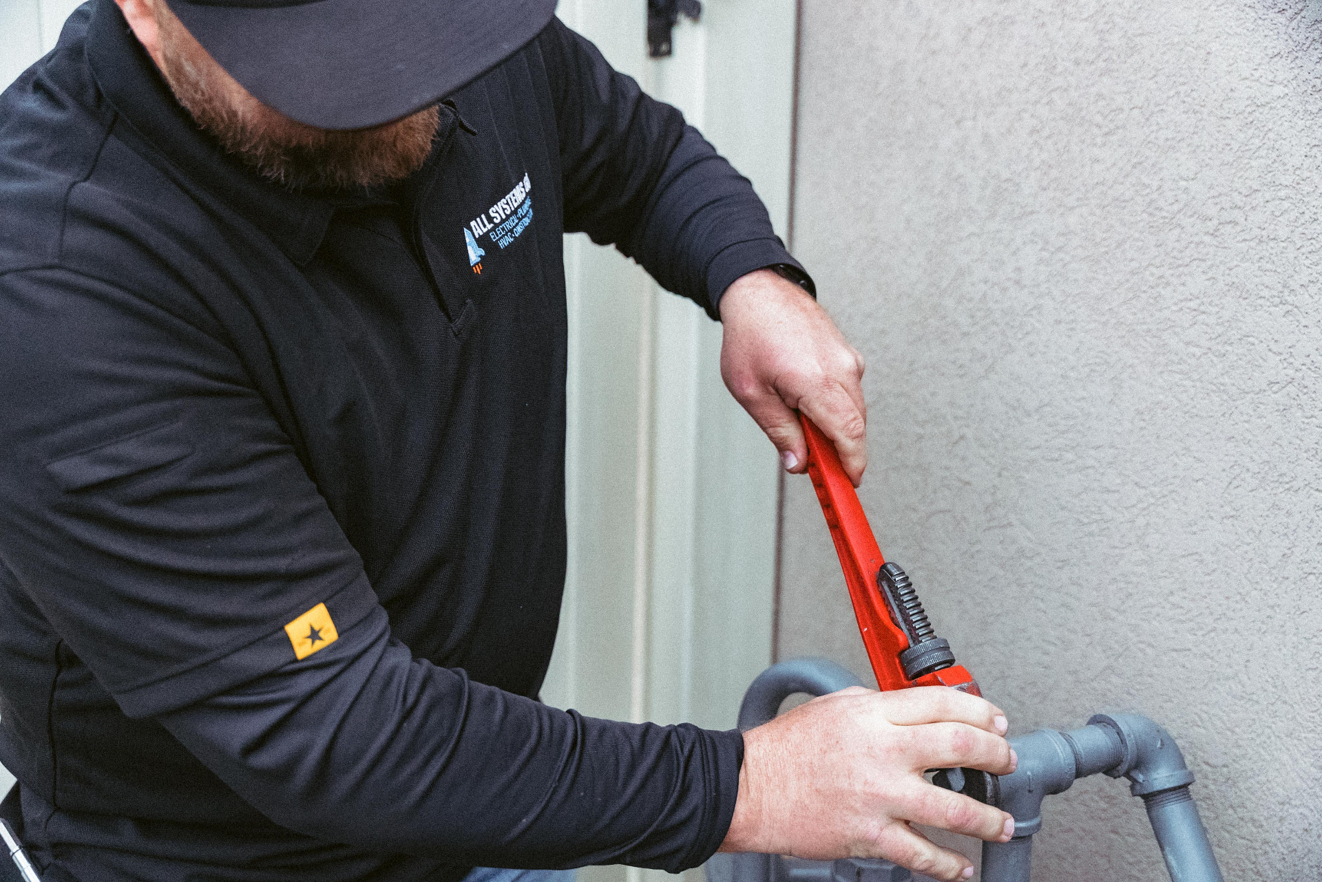 All Systems Go plumber tightening an exterior pipe with a large wrench