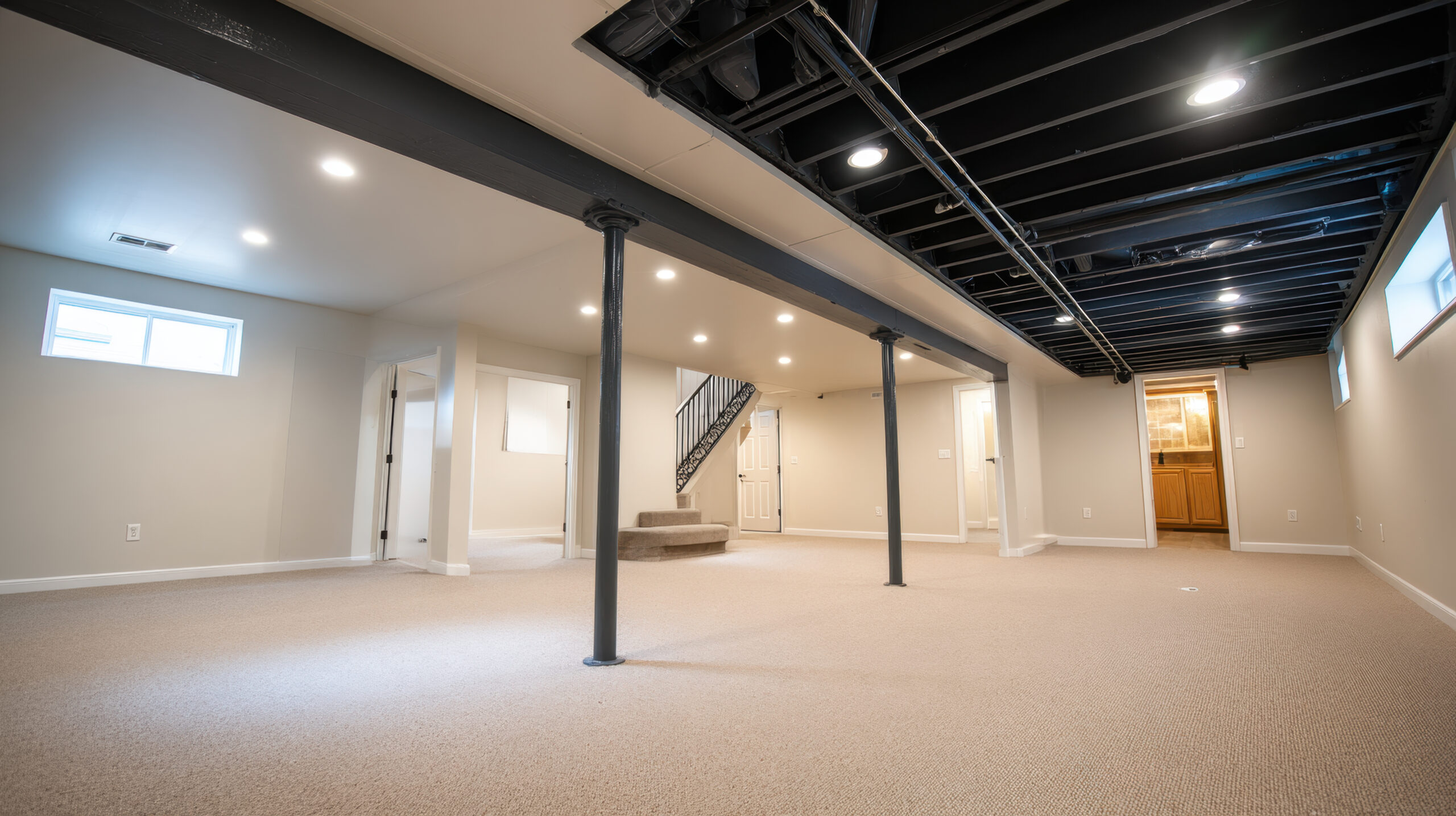 Spacious basement with modern lighting and structural support columns, featuring neutral color palette and multiple entry points, perfect for versatile use or renovation