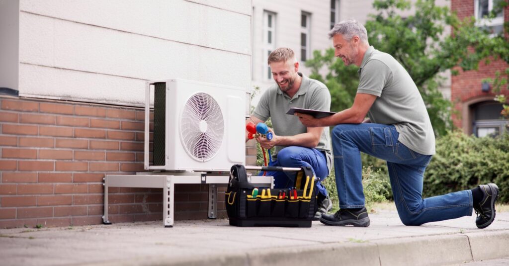 Two men repairing an air conditioner, focused on their task, with the phrase "All Systems Go" visible in the background.