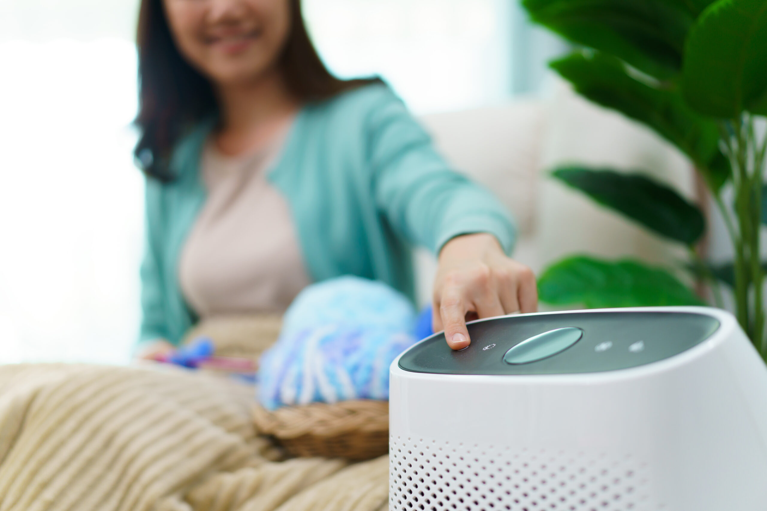 Happy Asian young woman turning on high efficiency air purifier while staying and relaxing in the living room. Woman using air purifier in her house.
